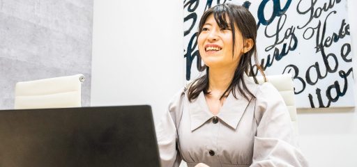ラップトップの前に座る、カジュアルなドレスを着た社員が、筆記体のアート装飾が施された洗練されたインテリアの背景の前で、インタビューを受けています。